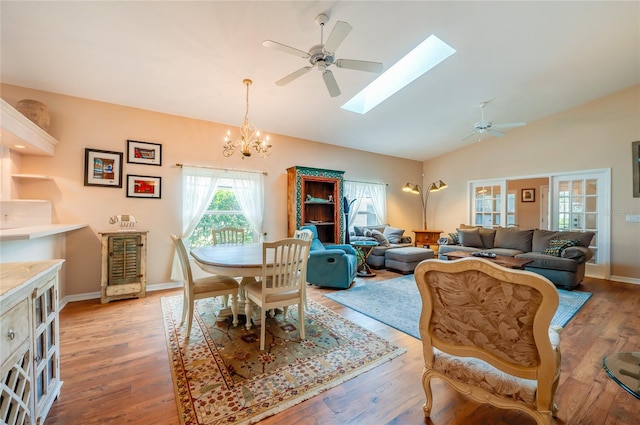 living room featuring lofted ceiling with skylight, light hardwood / wood-style floors, and ceiling fan with notable chandelier