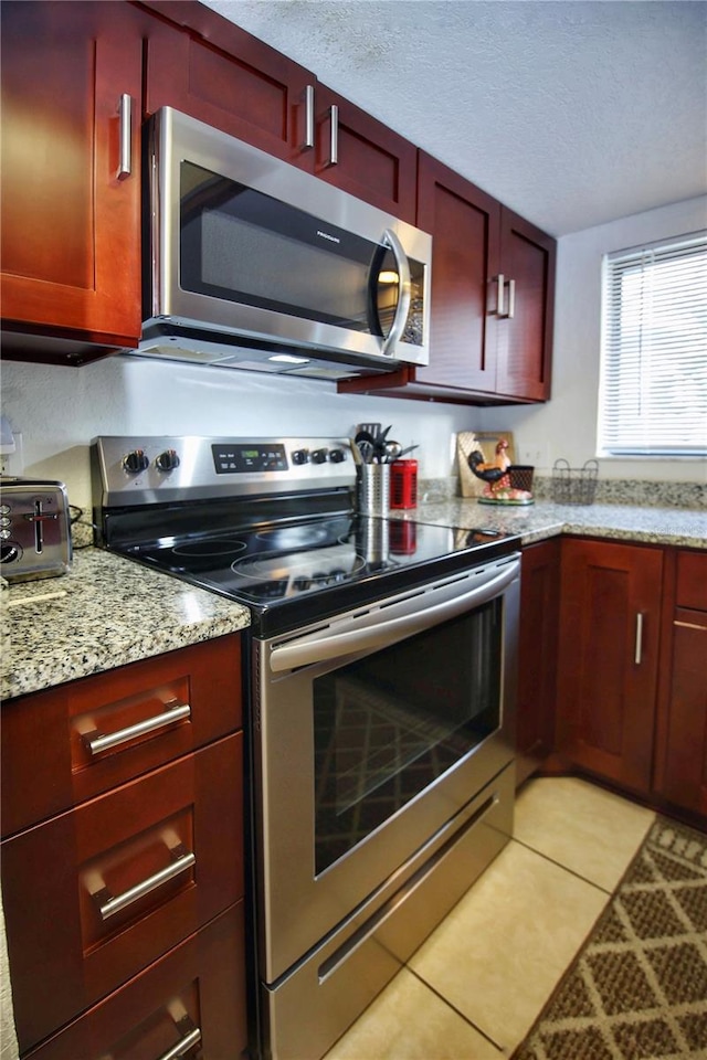 kitchen with a textured ceiling, light stone countertops, light tile floors, and appliances with stainless steel finishes