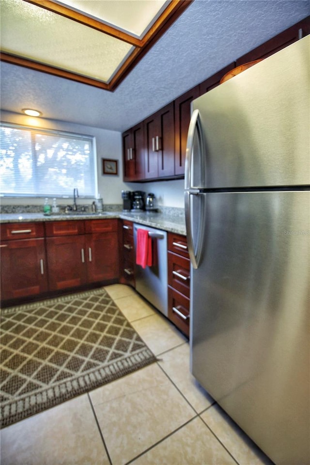 kitchen with light tile floors, a textured ceiling, appliances with stainless steel finishes, sink, and light stone counters