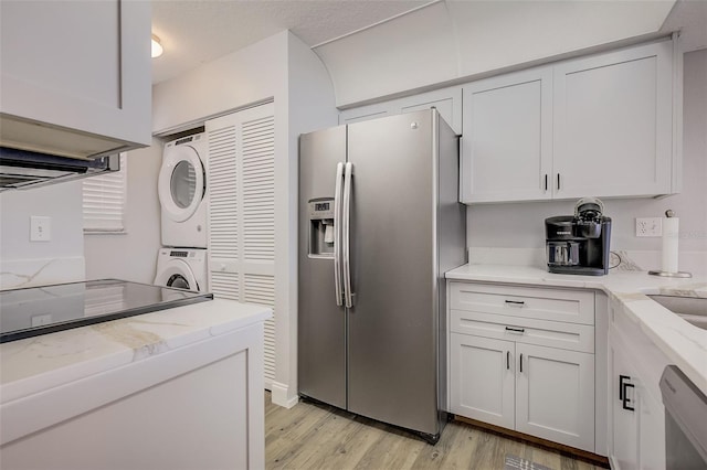 kitchen with white cabinetry, stacked washing maching and dryer, appliances with stainless steel finishes, and light hardwood / wood-style flooring