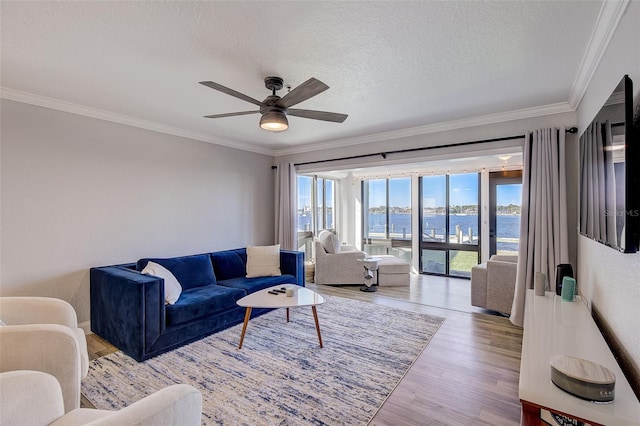 living room with ceiling fan, a textured ceiling, crown molding, a water view, and light wood-type flooring