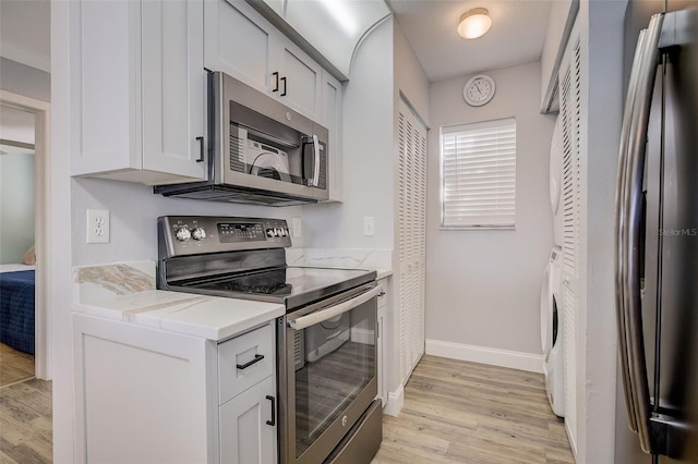 kitchen with white cabinets, light wood-type flooring, appliances with stainless steel finishes, and washer / dryer