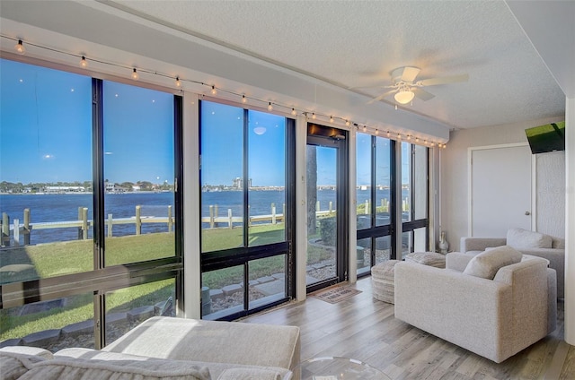 living room with rail lighting, a water view, ceiling fan, and light hardwood / wood-style flooring