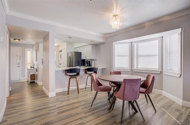 dining room featuring a textured ceiling, a chandelier, light hardwood / wood-style floors, and ornamental molding