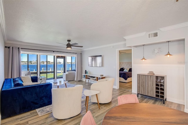 living room featuring ornamental molding, light hardwood / wood-style floors, ceiling fan, and a water view