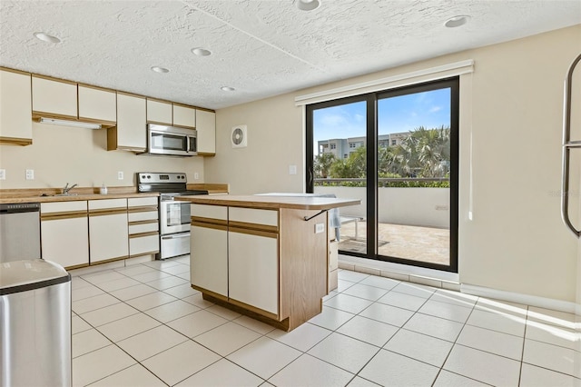 kitchen with white cabinetry, appliances with stainless steel finishes, light tile floors, a textured ceiling, and a kitchen island