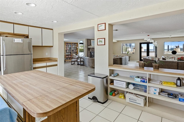 kitchen with stainless steel refrigerator, a textured ceiling, light tile flooring, and white cabinetry