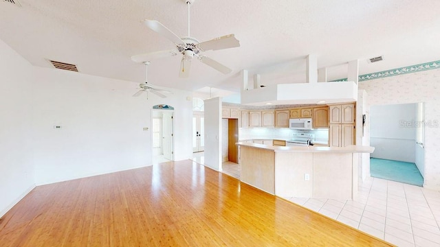 kitchen with a high ceiling, a kitchen island, ceiling fan, and light wood-type flooring