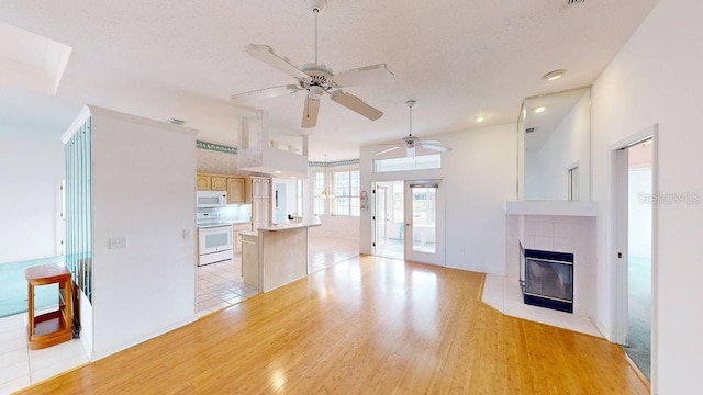 unfurnished living room featuring a tiled fireplace, french doors, ceiling fan, and light wood-type flooring