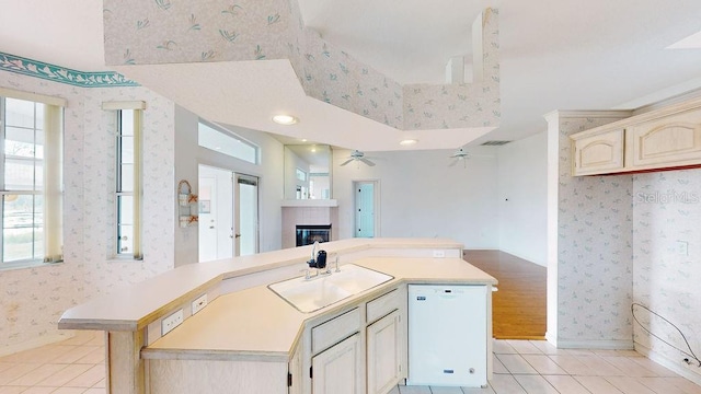 kitchen featuring ceiling fan, light tile floors, sink, white dishwasher, and a tiled fireplace