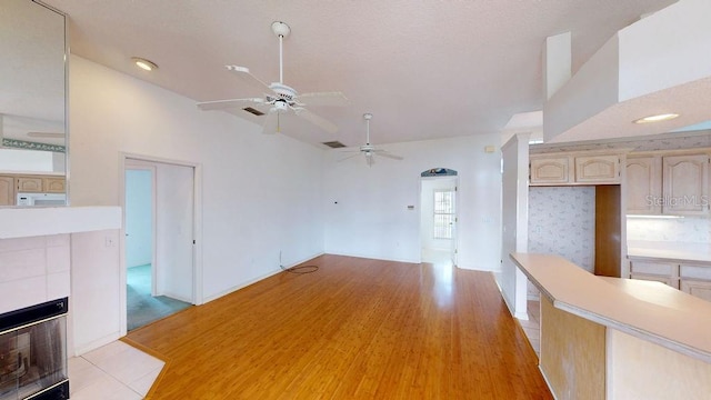 empty room featuring a tiled fireplace, ceiling fan, and light hardwood / wood-style flooring