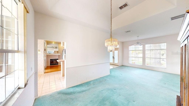 empty room with light tile flooring, ceiling fan with notable chandelier, a tray ceiling, and a high ceiling