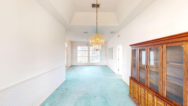 unfurnished living room featuring a high ceiling, a notable chandelier, light carpet, and a raised ceiling