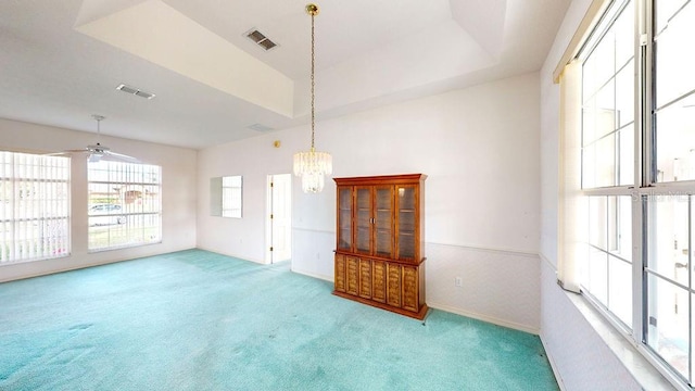 carpeted spare room with a raised ceiling and ceiling fan with notable chandelier