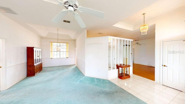 unfurnished room featuring a raised ceiling, ceiling fan with notable chandelier, and light tile floors