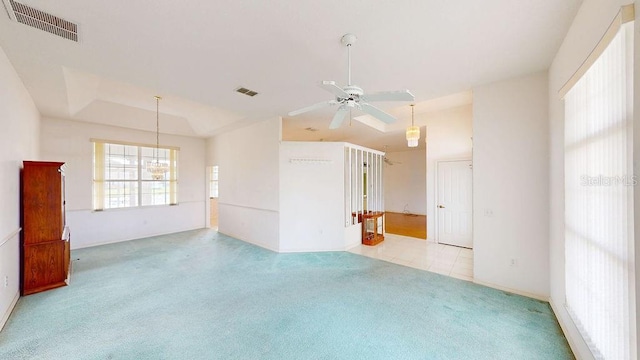 carpeted spare room with a tray ceiling and ceiling fan with notable chandelier