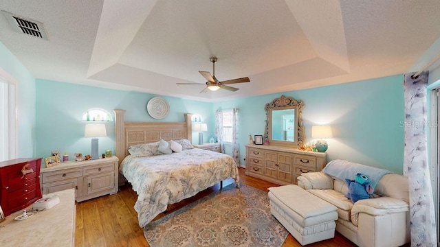 bedroom with a raised ceiling, light hardwood / wood-style floors, and ceiling fan