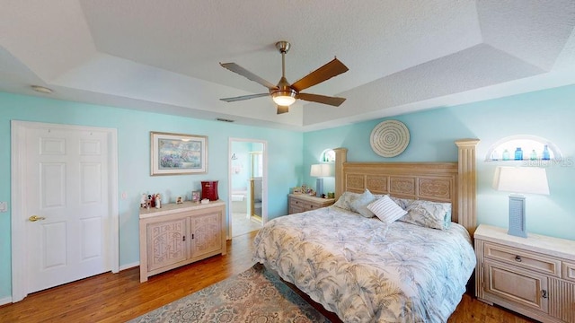 bedroom with a raised ceiling, light hardwood / wood-style floors, ceiling fan, and ensuite bathroom