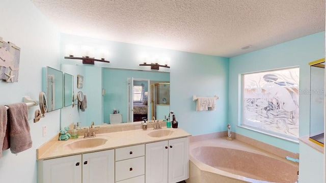 bathroom featuring dual vanity, a textured ceiling, and a bath to relax in