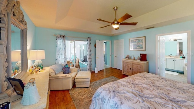 bedroom with connected bathroom, a tray ceiling, ceiling fan, and dark hardwood / wood-style floors