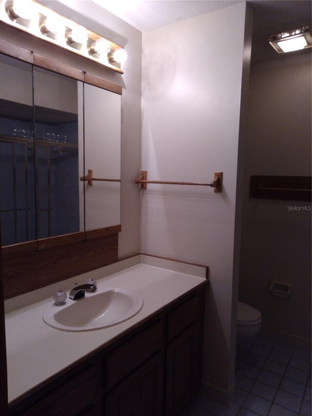 bathroom with toilet, vanity with extensive cabinet space, and tile flooring