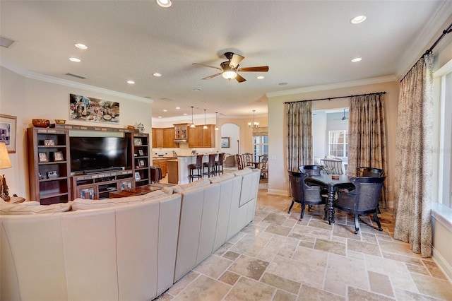 living room with light tile flooring, ornamental molding, ceiling fan with notable chandelier, and a wealth of natural light