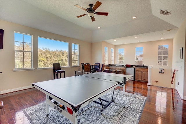 playroom with ceiling fan, a textured ceiling, a tray ceiling, and dark wood-type flooring