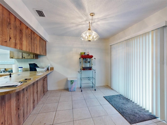 kitchen featuring light tile flooring, a textured ceiling, backsplash, hanging light fixtures, and an inviting chandelier