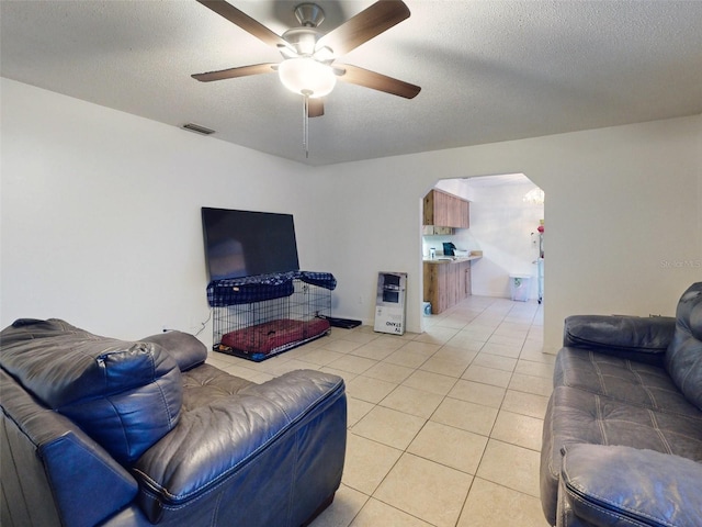 living room with a textured ceiling, light tile flooring, and ceiling fan