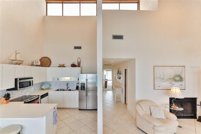 4875 S Atlantic Ave Unit E, New Smyrna Beach, FL 32169 - kitchen with light tile floors, appliances with stainless steel finishes, white cabinetry, and a towering ceiling