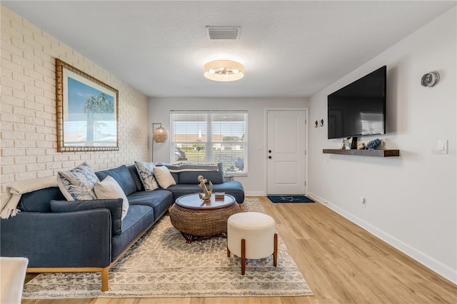 living room featuring brick wall, a textured ceiling, and light wood-type flooring