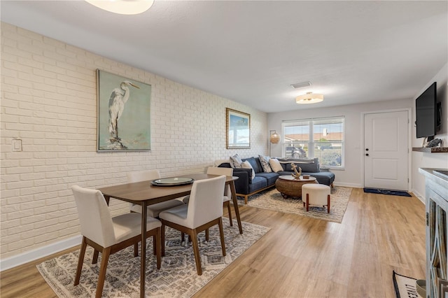 dining area with brick wall and light wood-type flooring