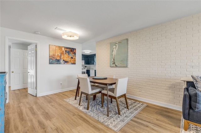 dining space featuring brick wall and light wood-type flooring