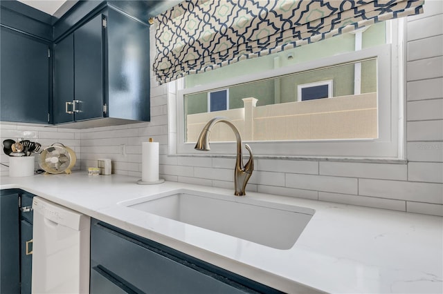 kitchen featuring sink, white dishwasher, blue cabinetry, backsplash, and light stone countertops