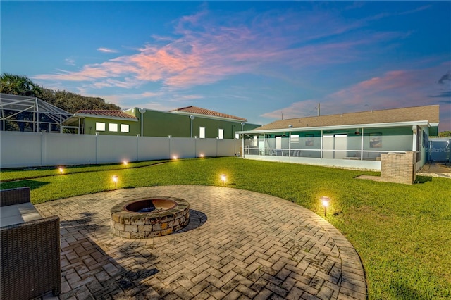 patio terrace at dusk with a fire pit, a lanai, and a lawn