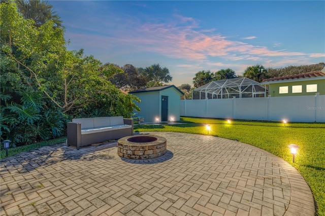 patio terrace at dusk featuring a shed, a fire pit, glass enclosure, and a yard