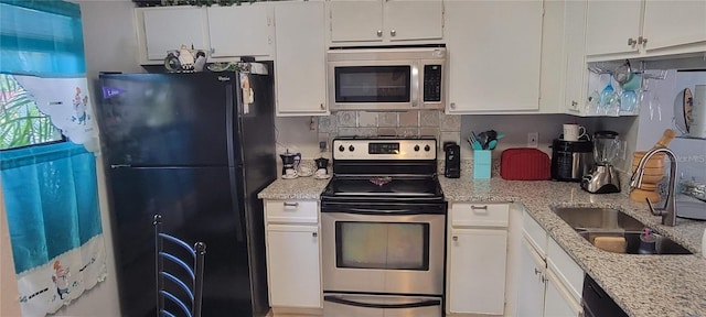 kitchen with appliances with stainless steel finishes, white cabinets, a sink, and tasteful backsplash