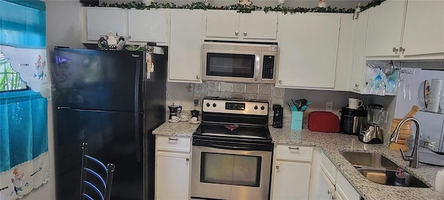 kitchen with appliances with stainless steel finishes, a sink, light stone counters, and white cabinets