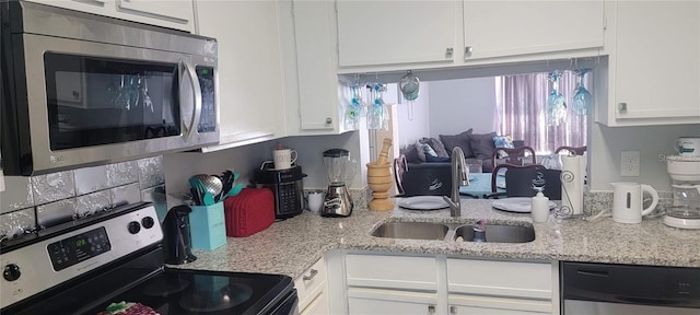 kitchen featuring appliances with stainless steel finishes, a sink, white cabinetry, and light stone countertops