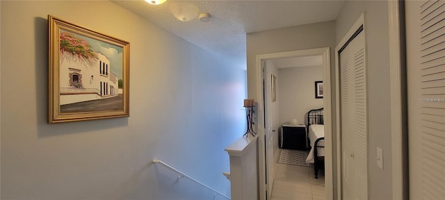 hallway with a textured ceiling, an upstairs landing, and tile patterned floors