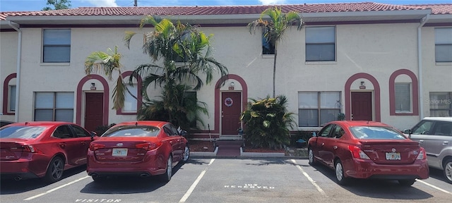 multi unit property featuring uncovered parking, a tiled roof, and stucco siding