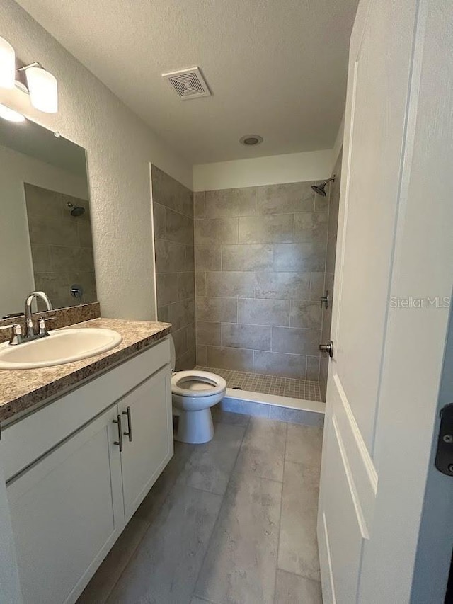 bathroom featuring a textured ceiling, toilet, vanity, and a tile shower