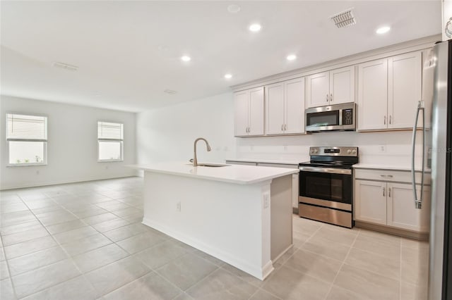 kitchen with stainless steel appliances, light countertops, visible vents, a sink, and an island with sink