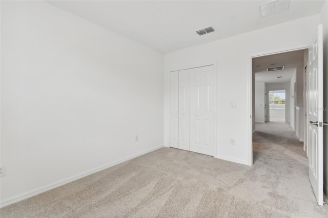 unfurnished bedroom with baseboards, visible vents, a closet, and light colored carpet