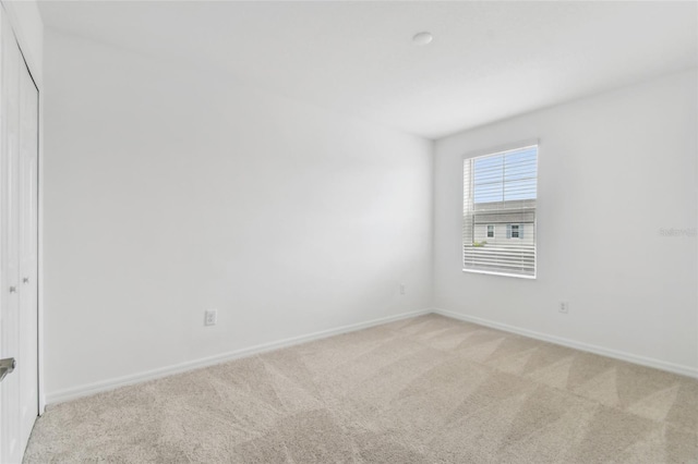 empty room featuring baseboards and light colored carpet