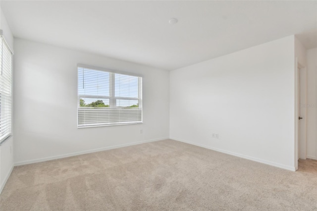 spare room featuring light colored carpet and baseboards