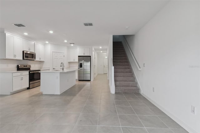 kitchen with appliances with stainless steel finishes, white cabinets, a center island with sink, light tile patterned flooring, and sink