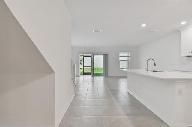 kitchen with baseboards, white cabinets, visible vents, light countertops, and a sink