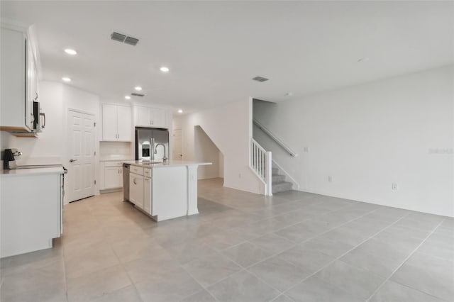 kitchen with appliances with stainless steel finishes, light tile patterned flooring, white cabinetry, and a kitchen island with sink