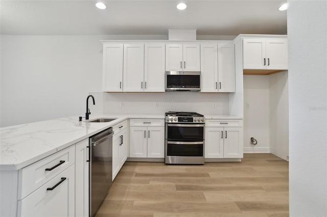 kitchen with appliances with stainless steel finishes, light stone counters, sink, light hardwood / wood-style flooring, and white cabinetry